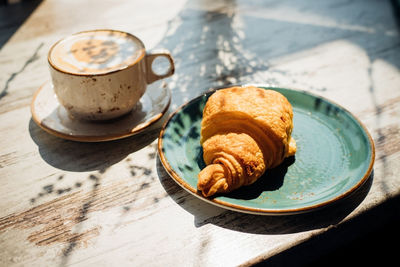Cappuccino and croissant are on the table in the cafe. morning sunlight falls on the table.