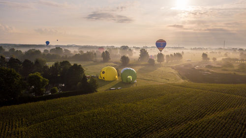 Hot air balloon flying over field against sky during sunset