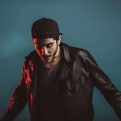 Young man wearing black jacket while standing against colored background