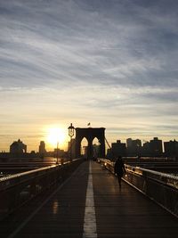 Silhouette woman walking on brooklyn bridge against sky during sunset