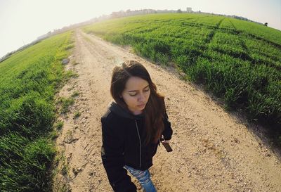 Fish-eye view of beautiful woman walking on dirt road amidst field