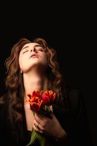 Portrait of young woman holding bouquet against black background