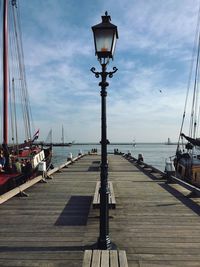 Sailboats on street by pier against sky
