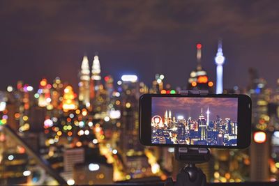 Close-up of mobile phone photographing against illuminated city at night