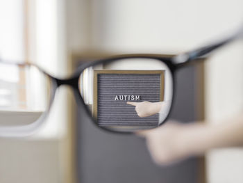 Kid points on grey letterboard with word autism. view through eyeglasses on medical diagnosis 