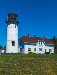 Lighthouse on field by buildings against blue sky