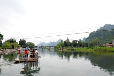 People standing on riverbank against clear sky