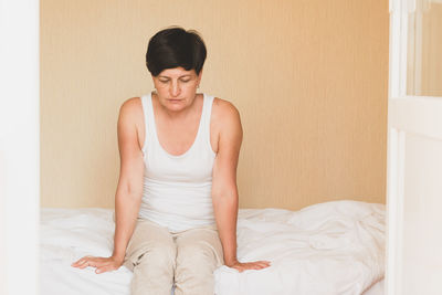 Side view of woman sitting on bed at home