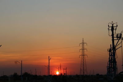 Silhouette electricity pylons against sky during sunset