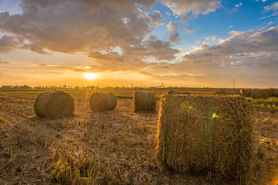 Hay bales on field against sky during sunset