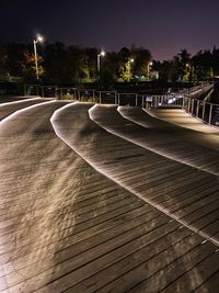 Empty road by illuminated city against sky at night