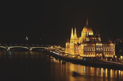 Illuminated hungarian parliament building by river against sky at night