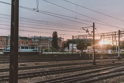 Train engine on railroad tracks by buildings against sky during sunset