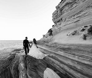 Rear view of wedding couple walking on rocky shore
