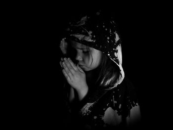 Girl with eyes closed praying while standing against black background