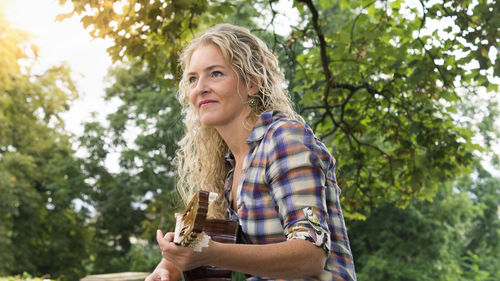 Portrait of smiling woman holding plants against trees