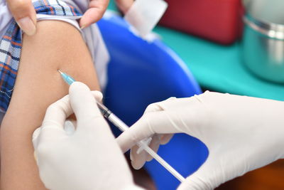 Cropped hand of doctor giving injection to patient at clinic