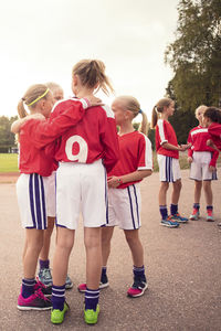 Soccer girls talking while standing on footpath against sky