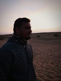 Young man looking away while standing on land against sky during sunset