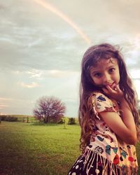 Portrait of girl standing on grass against rainbow in sky