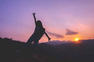 Silhouette of woman enjoying the sunset with dramatic sky on mountain peak.