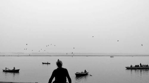 Woman looking at view while sitting against lake and clear sky