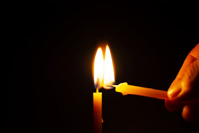 Close-up of hand holding lit candle against black background