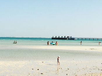 People on calm beach against clear sky