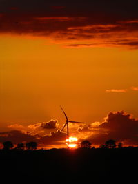 Silhouette of wind turbine against cloudy sky during sunset