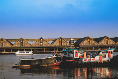 Boats moored in river by houses against blue sky