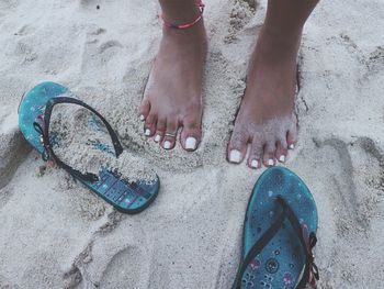 Low section of woman standing at beach by slippers