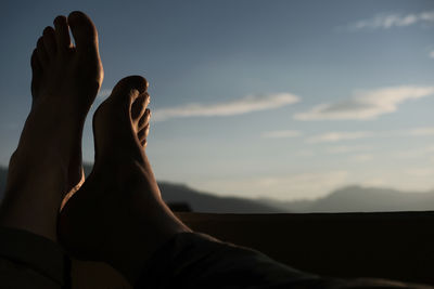 Low section of man with feet up against sky