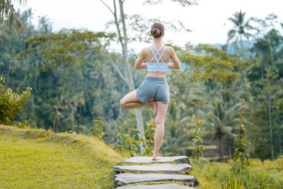 Rear view of woman exercising on rock in park