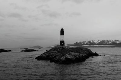 Lighthouse on rock in sea against sky during winter