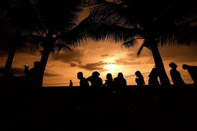 Silhouette people standing by palm trees against sky during sunset