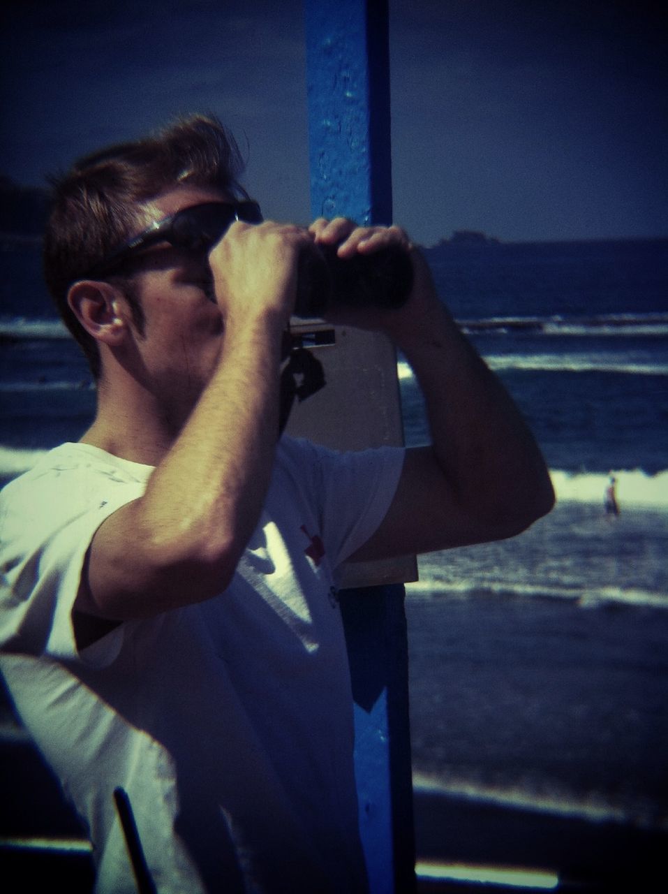 lifestyles, young adult, leisure activity, person, young men, three quarter length, casual clothing, sitting, side view, holding, technology, sunlight, full length, standing, sea, photographing, wireless technology