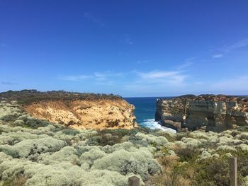 Rock formations by sea against blue sky