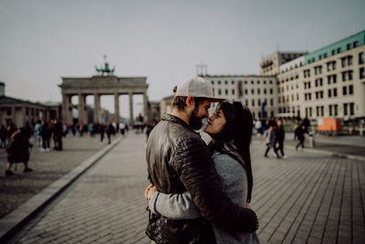 Side view of couple romancing while standing on street in city