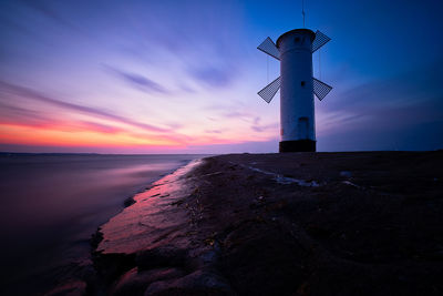 Traditional windmill at beach against sky during sunset