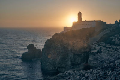 Lighthouse by sea against sky during sunset