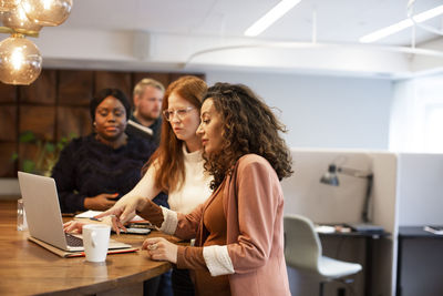 Pregnant businesswoman discussing with colleagues over laptop at office