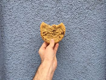 Cropped image of man holding cookie against wall