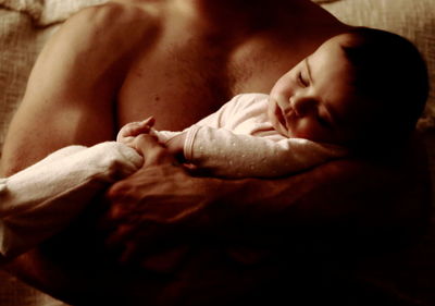 Midsection of shirtless man holding son at home