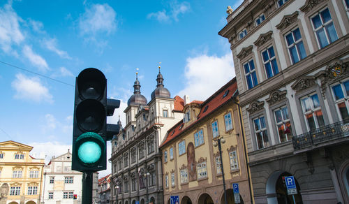 Low angle view of road signal by buildings against sky