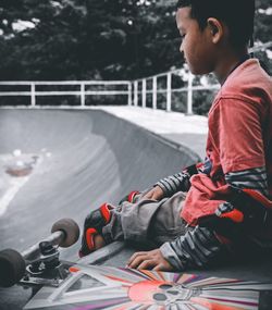 Side view of boy sitting at skateboard park