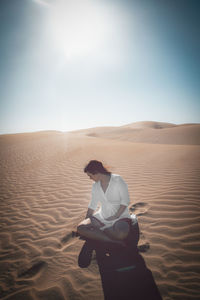 Man on sand dune in desert against sky