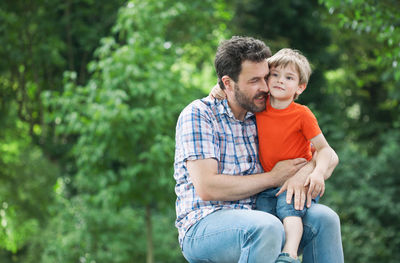 Portrait of father with son sitting against trees