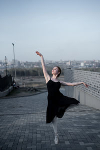 Full length of woman dancing against sky in city