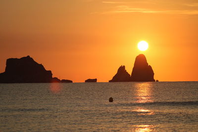 Silhouette rock formation in sea against sky during sunset