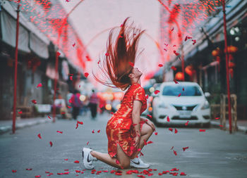 Full length side view of young woman tossing hair on street in city